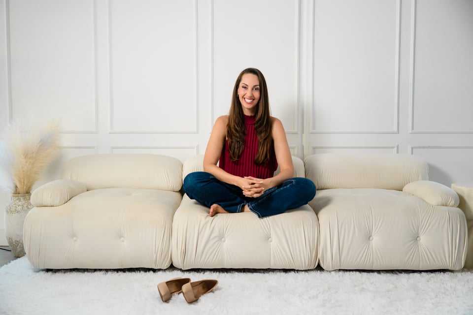 Vanessa Van Edwards sitting cross-legged barefoot on cream sofa