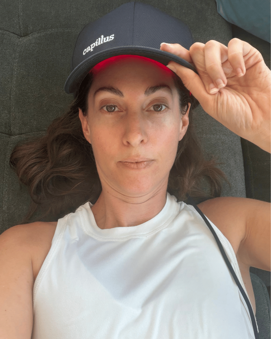 A red-light therapy cap worn indoors, its red LEDs glowing under the brim.