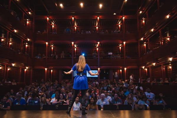 Vanessa Van Edwards on stage with arms wide open facing packed theater