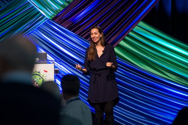 Vanessa Van Edwards speaking at conference with video screen backdrop