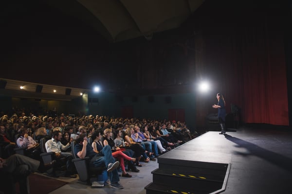 Vanessa Van Edwards speaking to large audience in darkened auditorium