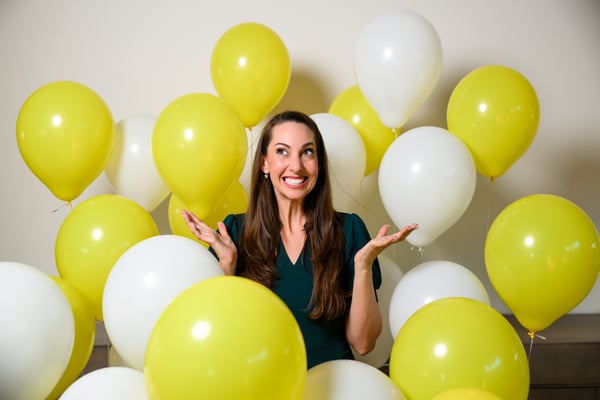 Vanessa Van Edwards shrugging playfully among yellow balloons