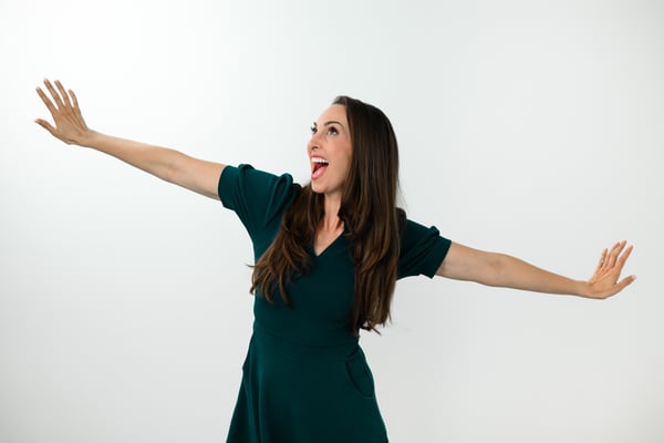 Vanessa Van Edwards in teal dress with arms spread expressively