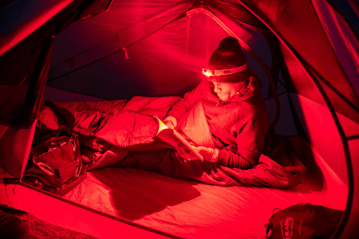 An image of a man in a tent using a red headlamp which can impact your melatonin release and circadian rhythms. This is an example of color psychology.
