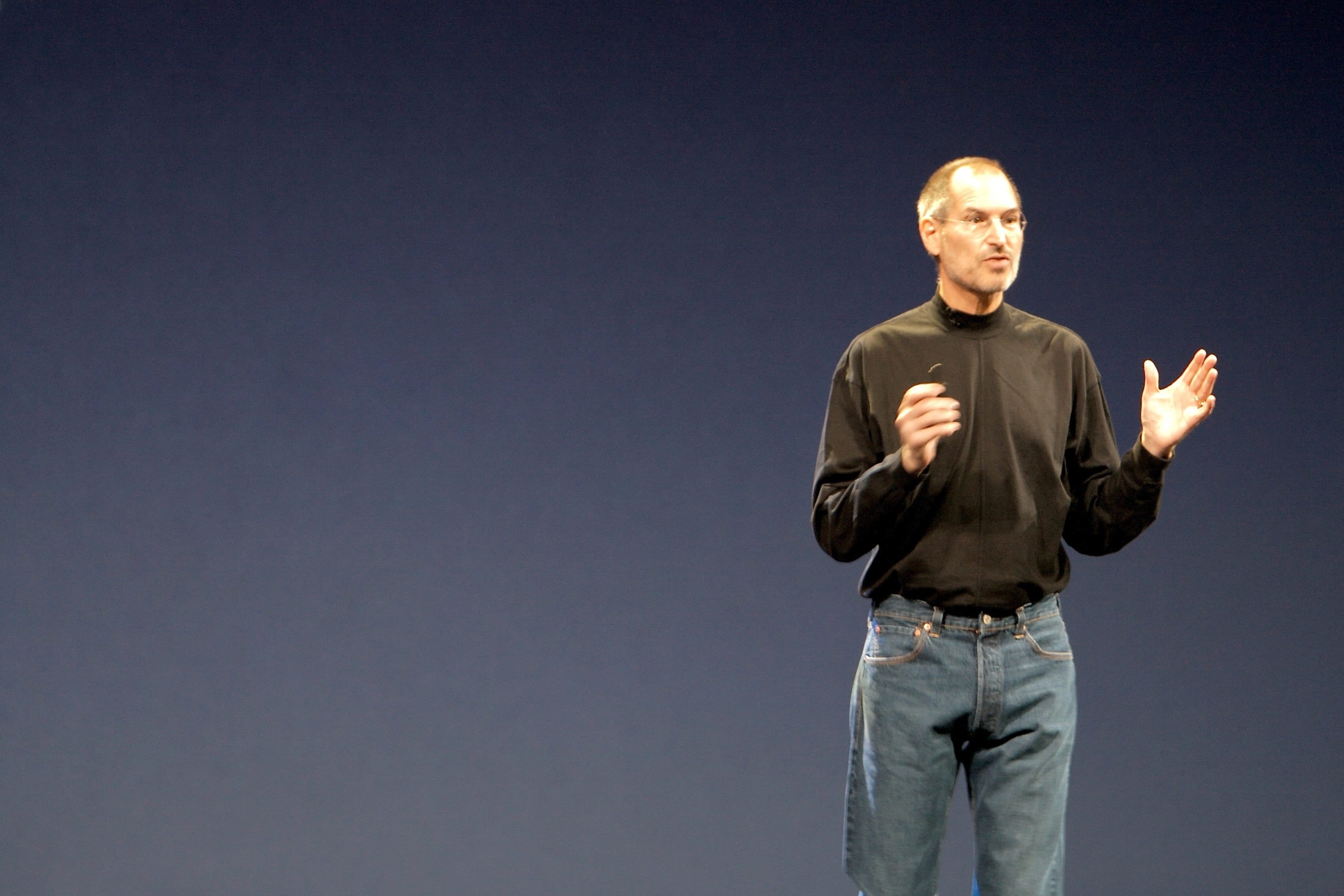 Steve Jobs gives a presentation while wearing a black turtleneck on stage.