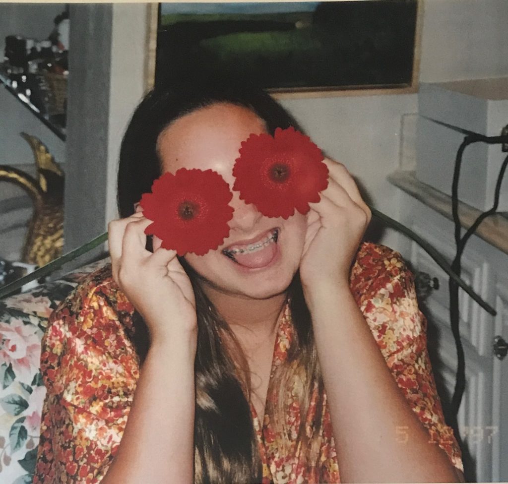 Young Vanessa trying to hide from her awkwardness holding flowers in front of her eyes