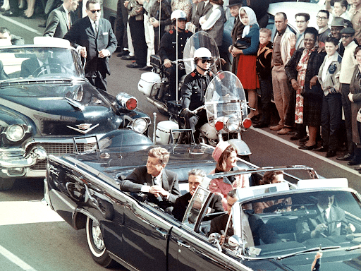 An image of president John F. Kennedy in a six-seater car before he was assassinated. Most people remember it being four seats, which is an example of the mandela effect.