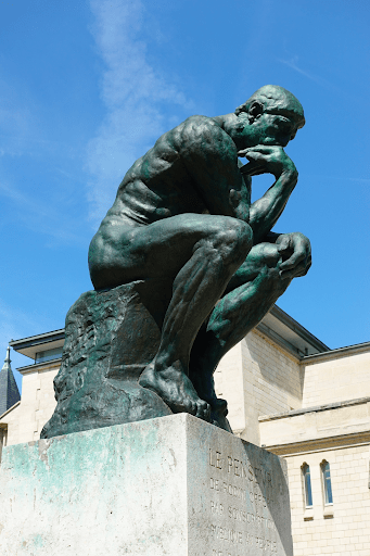 The Thinker statue of a man thinking, with the back of his hand resting on his chin. Most people remember him in a classic thinking pose with a fist to his chin, which is an example of the mandela effect.