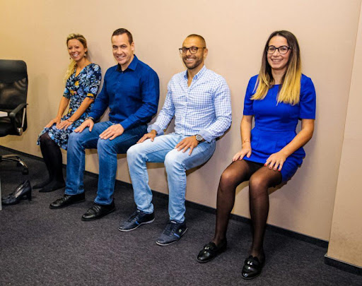 A group of four coworkers are practicing office sits on the wall as an office exercise