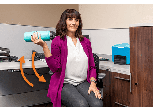 A woman is sitting at her desk doing bicep curls with a water bottle as an office exercise