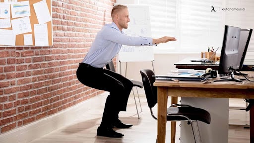 A man is at work in a suit doing chair squats as an office exercise
