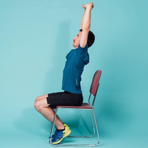 Man is sitting in a chair reaching his arms up in a stretch as an office exercise