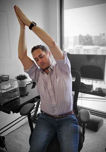 A man is at work doing a crescent moon pose stretch as an office exercise