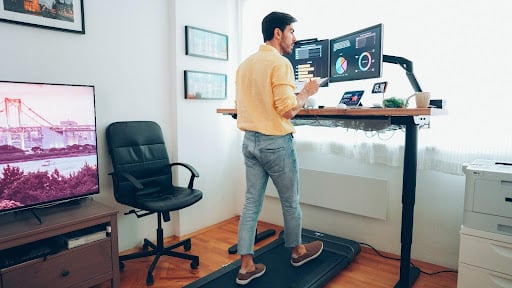 A man is working from home looking at a computer screen while walking on a treadmill as an office exercise