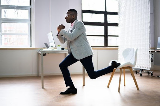 A man is at work doing office split squats in a suit as an office exercise
