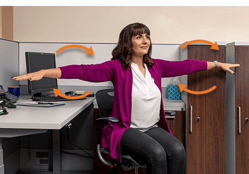A woman is at work doing arm circles in her chair as an office exercise