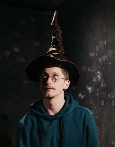 A man with a Harry Potter hat on, looking up, which is referring to a Harry Potter-themed game where you put on your sorting hat and see which Hogwarts house you belong to. You take turns asking Harry Potter trivia questions and award points to the team that answers correctly.  It makes a great party game.