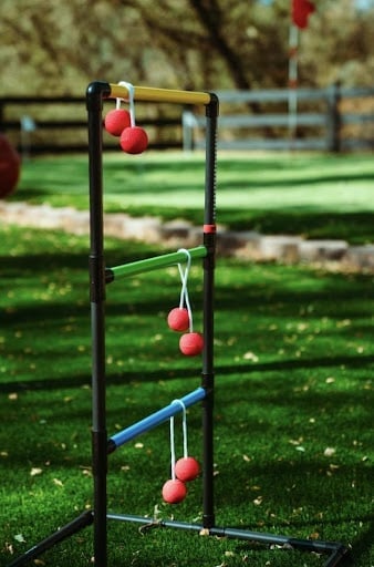 An image of the game ladder toss, which makes a great party game. The objective of the game is to toss your bolas, which are two balls connected by a string, onto the rungs of a ladder. The higher the rung that your bola lands on, the more points you will score. 