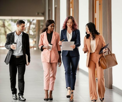 An example of formal office dress code, the color scheme is typically neutral, with only black, gray, or tan colors and few patterns. For men, formal office attire is straightforward: a tailored suit, dress shirt, tie, and closed-toe dress shoes. The image demonstrates one man and three women showing off this dress code.