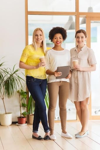 An example of three women wearing semi-casual or smart casual office dress code. This more relaxed dress code allows for casual and semi-formal elements. Women can wear blouses, sleeveless tailored shirts, skirts, or jeans with comfortable but neat shoes or sandals.